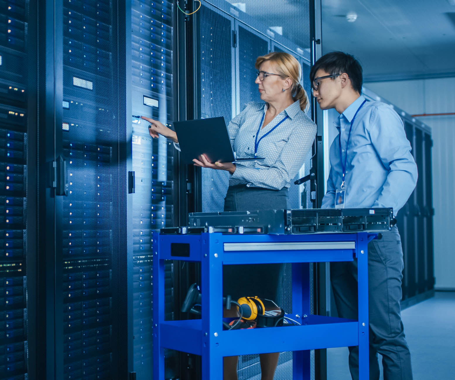 In the Modern Data Center: Engineer and IT Specialist Work with Server Racks, on a Pushcart Equipment for Installing New Hardware. Specialists Doing Maintenance and Diagnostics of the Database.